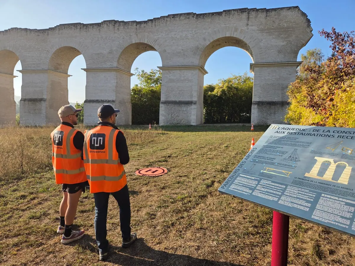 Deux stagiaires en gilet Minute Drone devant un aqueduc