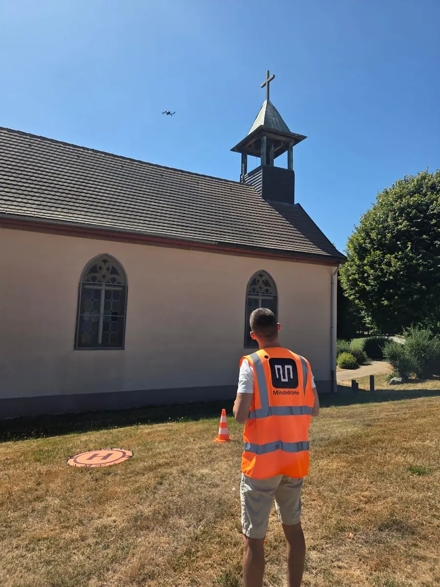 Stagiaire pilotant un drone devant une chapelle