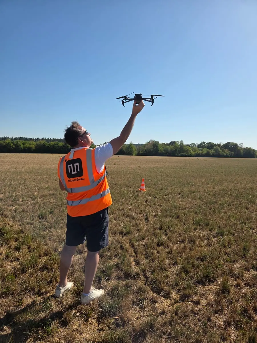 Stagiaire tenant un drone à bout de bras dans un champ